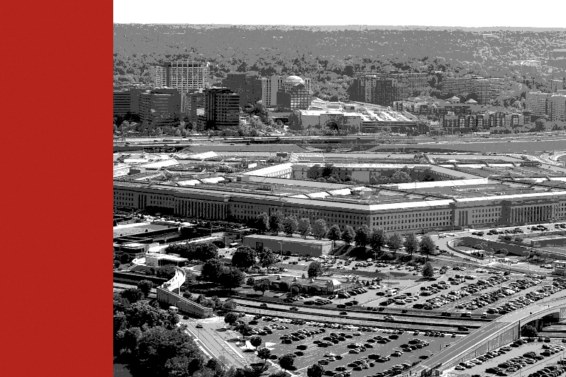 The Pentagon seen from the air, its parking lots in the foreground and office towers behind, in near black and white with a flat red bar down the left edge of the frame