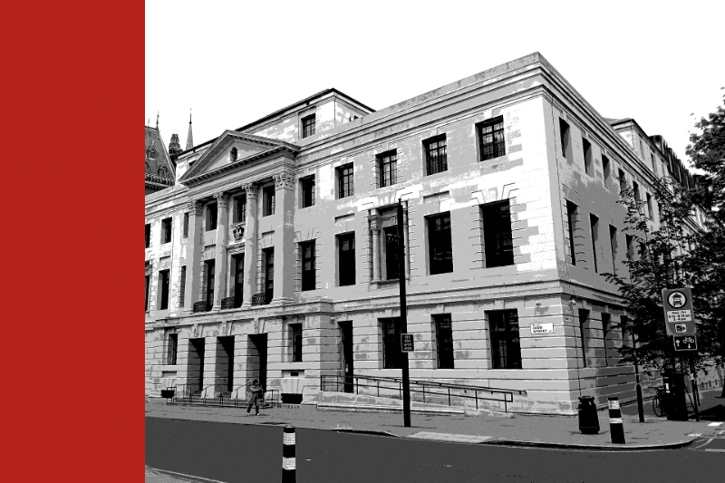 Camden Town Hall on Euston Road in London, a pale stone building with columns along its upper floors on a street corner, in near black and white with a flat red band down the left edge