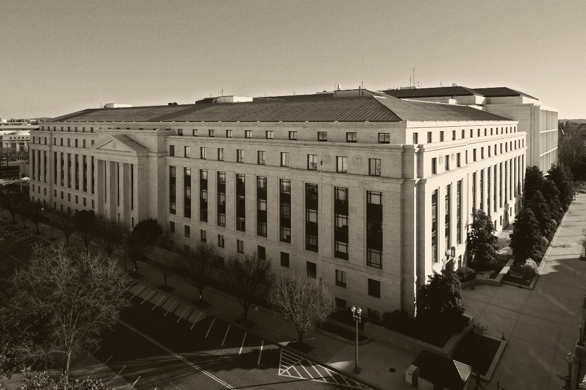 The Dirksen Senate Office Building in Washington seen from above, a long pale stone building with a green copper roof beside a tree-lined street under a clear sky, in an ink and bone duotone