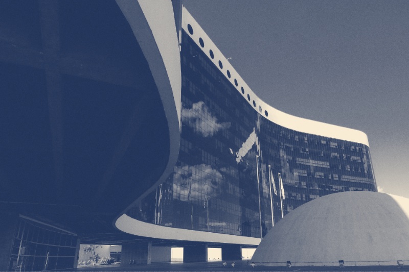 The curved glass tower of Brazil's electoral court in Brasília beside a low white concrete dome, in a slate and bone duotone