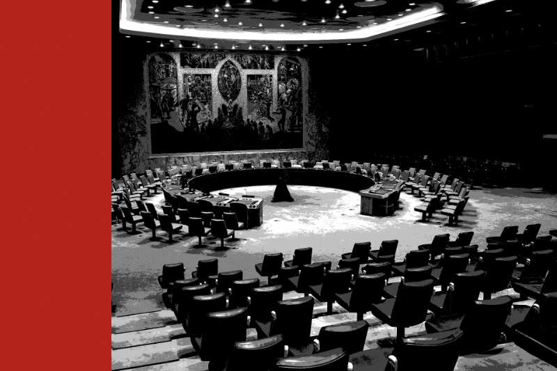 The horseshoe table of the United Nations Security Council chamber beneath its mural, rows of empty seats in the foreground, in near black and white with a flat red bar down the left edge of the frame