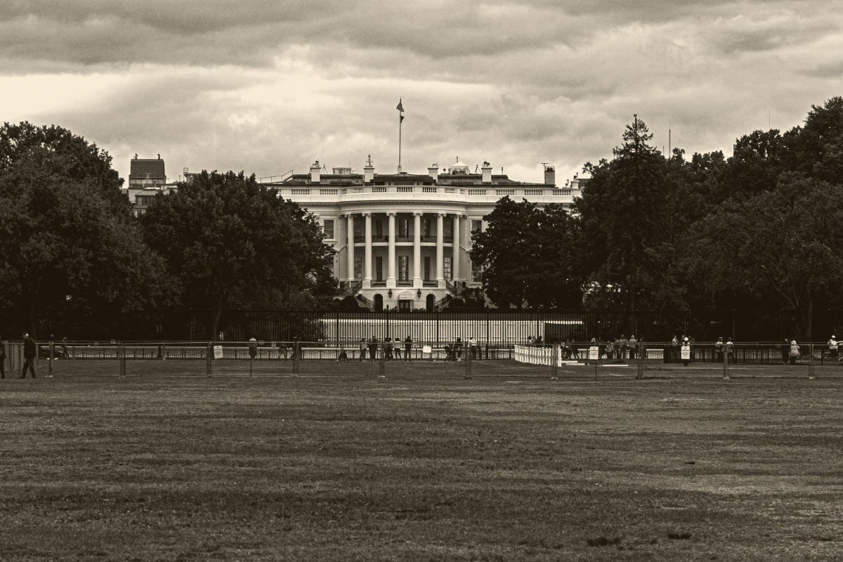 The White House seen across the Ellipse from behind the security fence on a heavy grey afternoon, in an ink and bone duotone