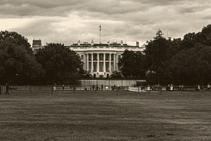 The White House seen across the Ellipse from behind the security fence on a heavy grey afternoon, in an ink and bone duotone