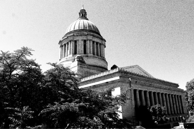The dome and colonnaded flank of Washington's Legislative Building in Olympia rising above trees, in high contrast black and white with coarse grain