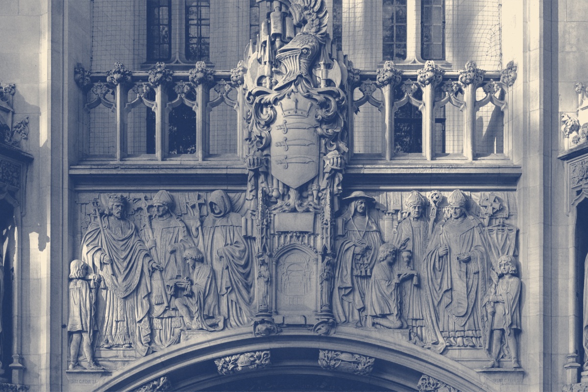 The carved stone entrance of Middlesex Guildhall in London, home of the UK Supreme Court, with sculpted figures and a heraldic shield above the arch, in a slate and bone duotone