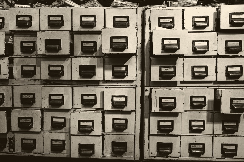 A wall of pale card index drawers with metal pulls and label holders, in an ink and bone duotone