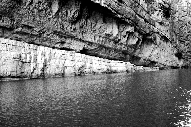 The pale limestone walls of Santa Elena Canyon rising from the still water of the Rio Grande, in high contrast black and white with coarse grain