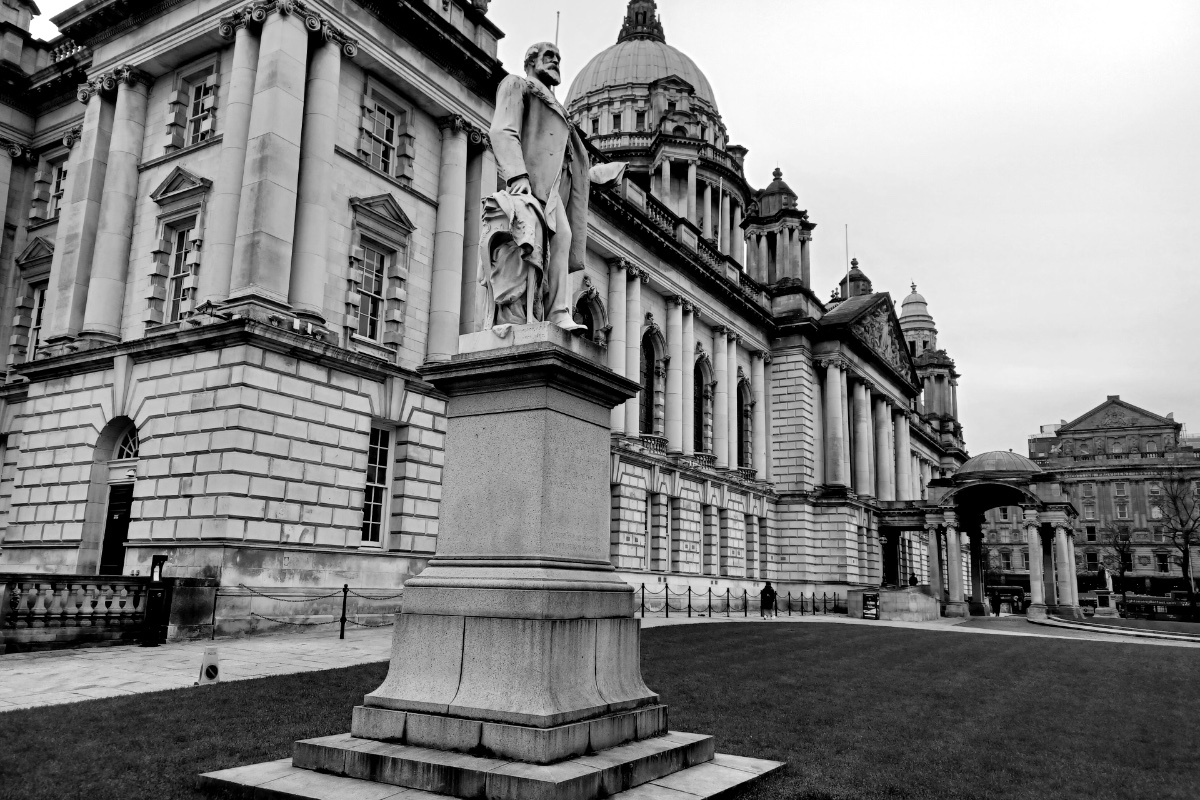 Belfast City Hall and its domes behind a statue on a stone plinth in the lawn, in plain black and white