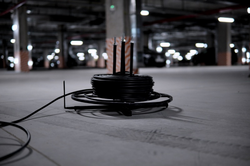 A coil of heavy black cable on a spool in a parking structure