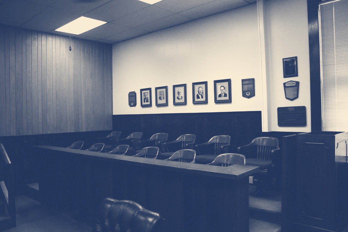 The empty jury box of a county courthouse, rows of wooden chairs behind a wooden rail