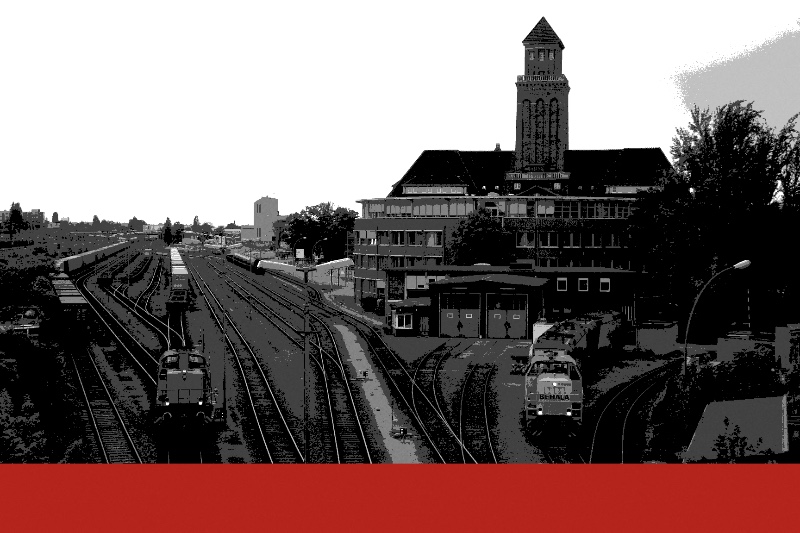 Rail sidings at Berlin’s Westhafen with diesel shunting locomotives on the tracks and a brick administration building with a clock tower behind, in near black and white with a flat red band along the foot of the frame