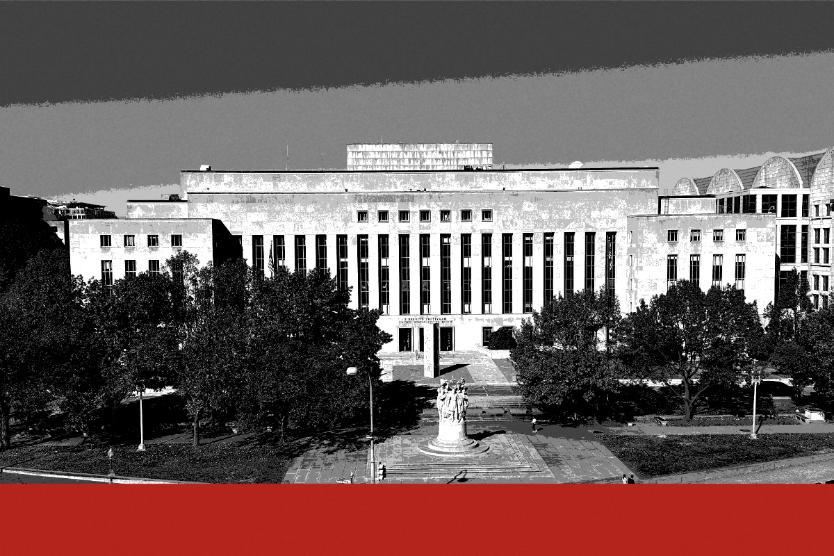 The E. Barrett Prettyman courthouse in Washington seen from above, a long pale stone building with a flat roofline behind a small park and a monument, in near black and white with a flat red band along the foot of the frame