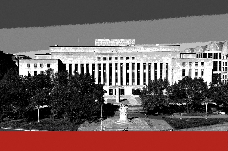 The E. Barrett Prettyman courthouse in Washington seen from above, a long pale stone building with a flat roofline behind a small park and a monument, in near black and white with a flat red band along the foot of the frame