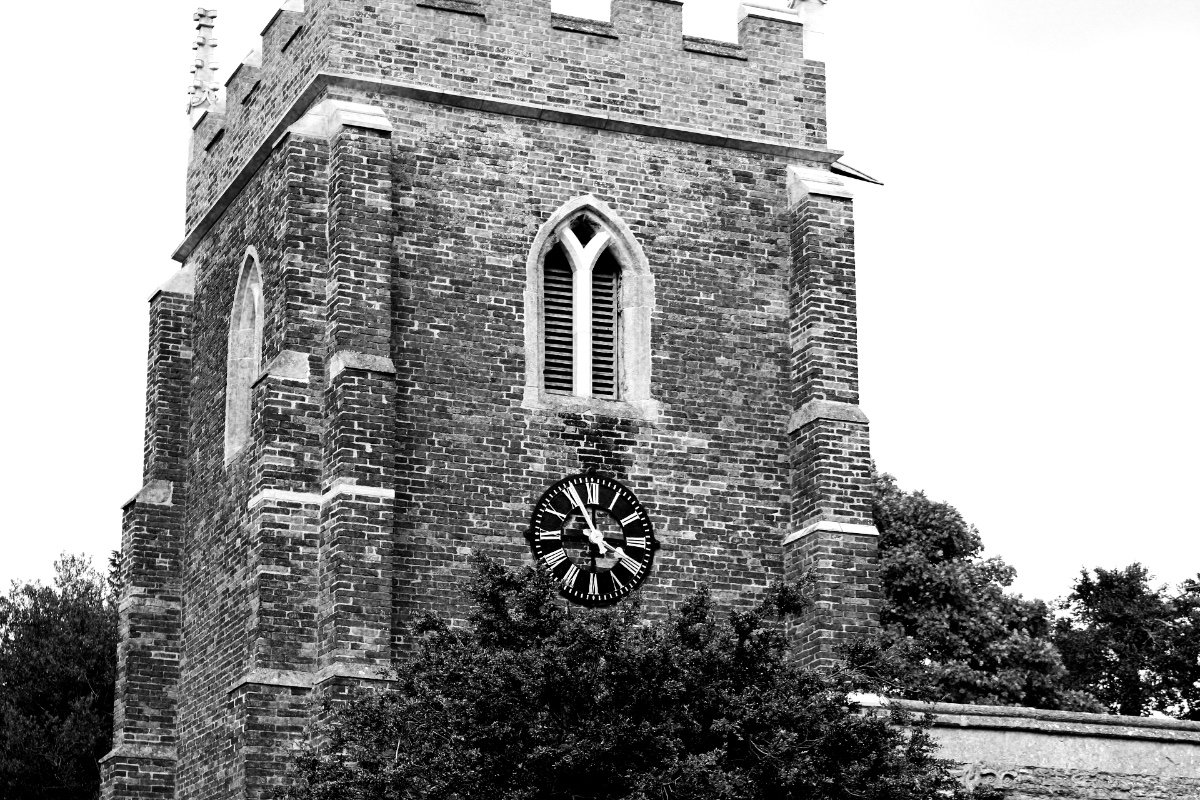 A brick church tower with a clock face, in high contrast black and white with coarse grain