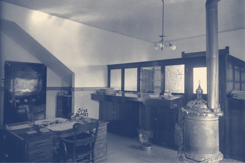 The interior of an 1890s office with desks and a stove, in a blue duotone