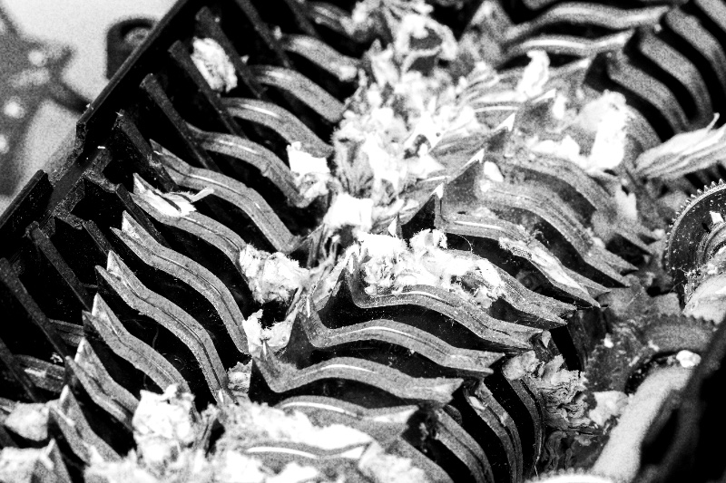 Close view of shredded paper caught in the cutting blades of a paper shredder, in high contrast black and white with coarse grain