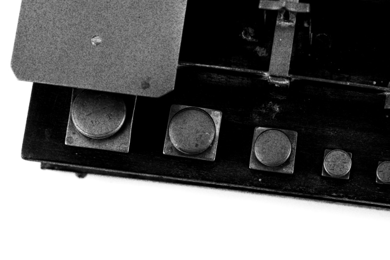 A letter balance with graduated brass weights on a wooden base, in high contrast black and white with coarse grain