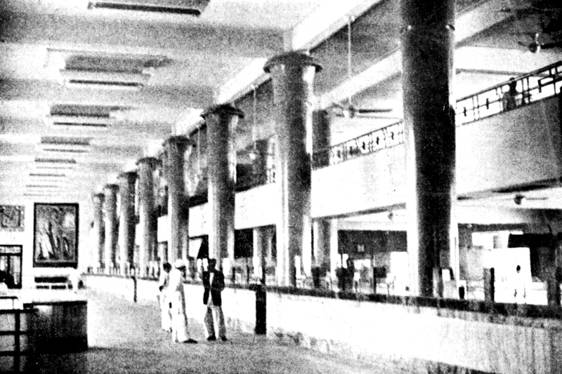 The colonnaded interior of a 1950s banking hall, in high contrast black and white with coarse grain