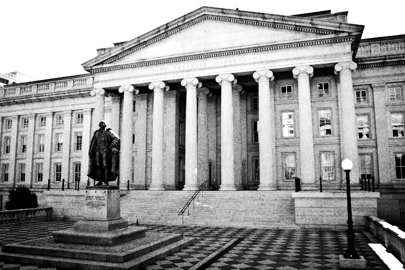 The colonnaded front of the US Treasury Building in Washington with a statue before its steps, in high contrast black and white with coarse grain