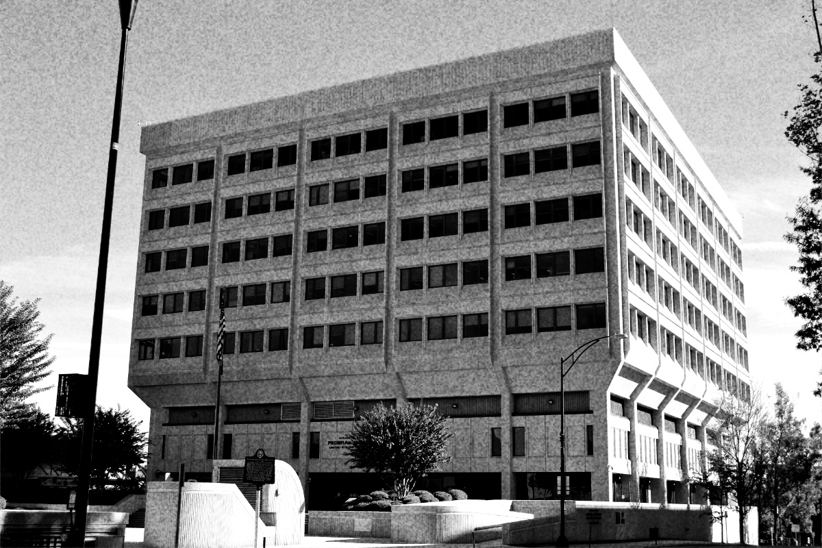 The Hiram H. Ward Federal Building and U.S. Courthouse in Winston-Salem, a pale concrete block of ribbon windows over a recessed ground floor, seen from an empty plaza with trees and lamp posts, in grainy high-contrast black and white