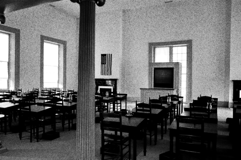 A restored nineteenth century legislative chamber with desks and chairs, in high contrast black and white with coarse grain