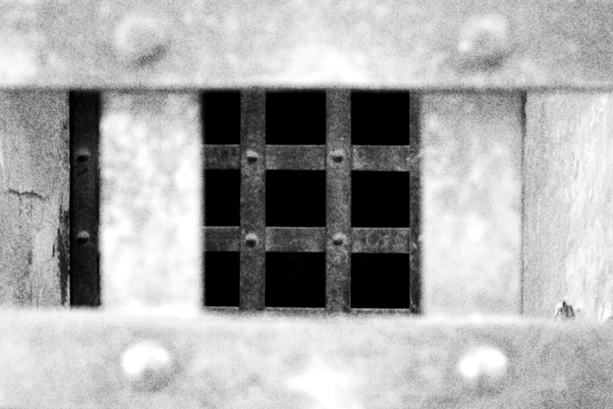 A close view of rusted iron prison cell door bars, in high contrast black and white with coarse grain
