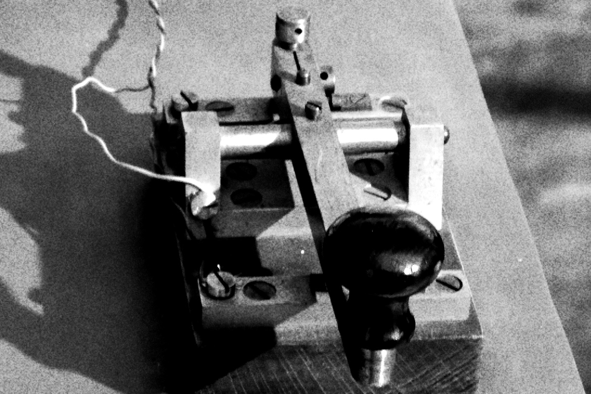 A brass telegraph key on a wooden base, in high contrast black and white with coarse grain