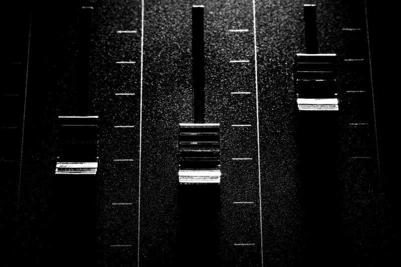 The faders of an audio mixing console in close view, in high contrast black and white with coarse grain
