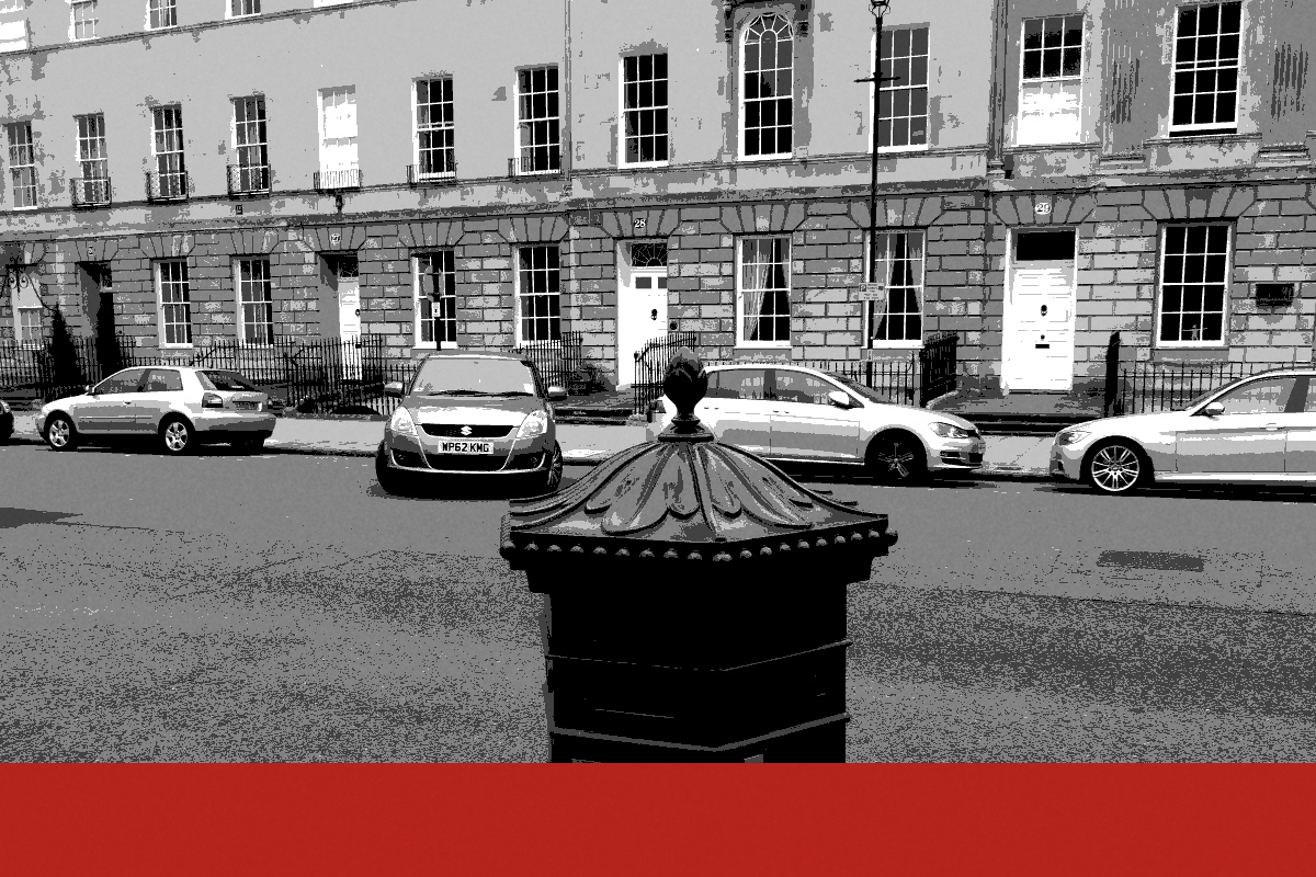 A red Victorian hexagonal pillar box on a street, banded in the house treatment