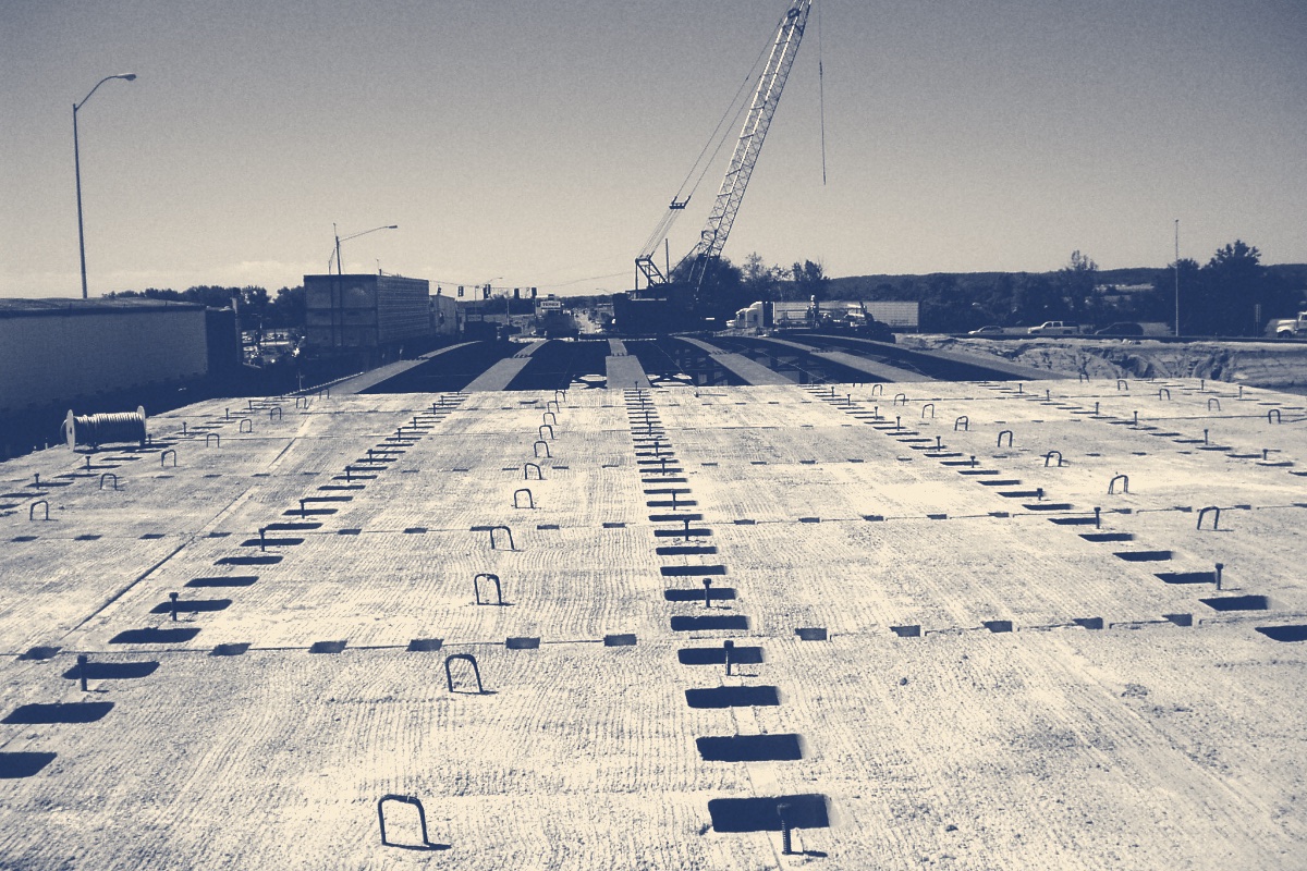 A bridge deck under construction with a crane on the roadway, in a blue duotone