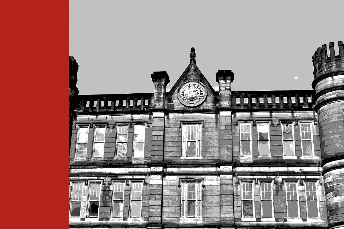 The stone facade of a nineteenth century penitentiary with turrets and a clock, banded in the house treatment