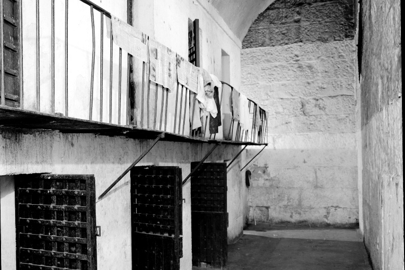 A jail cell block with an iron catwalk and barred doors, in plain black and white