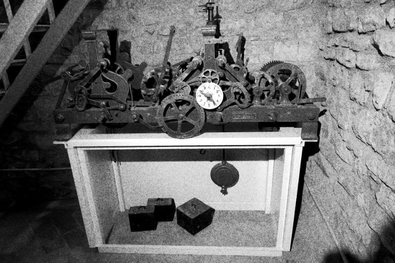 The exposed gearing of an old tower clock movement, in high contrast black and white with coarse grain