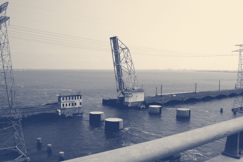 A raised bascule drawbridge over open water, in a blue duotone
