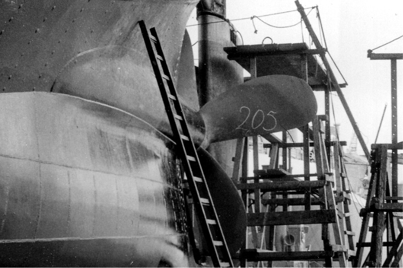 The stern of a ship in dry dock with ladders and scaffolding, in plain black and white