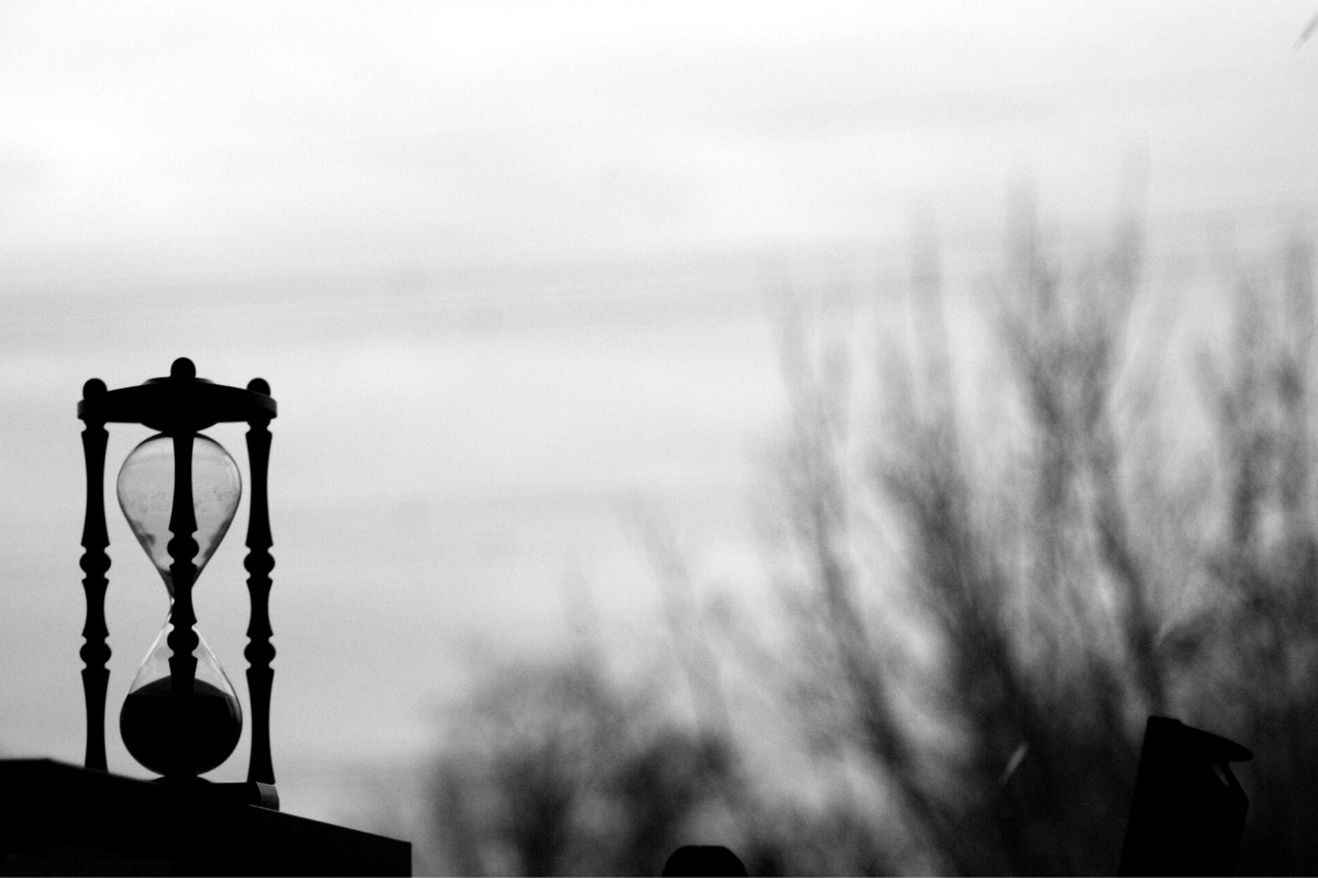 An hourglass on a wall against an overcast sky, in plain black and white