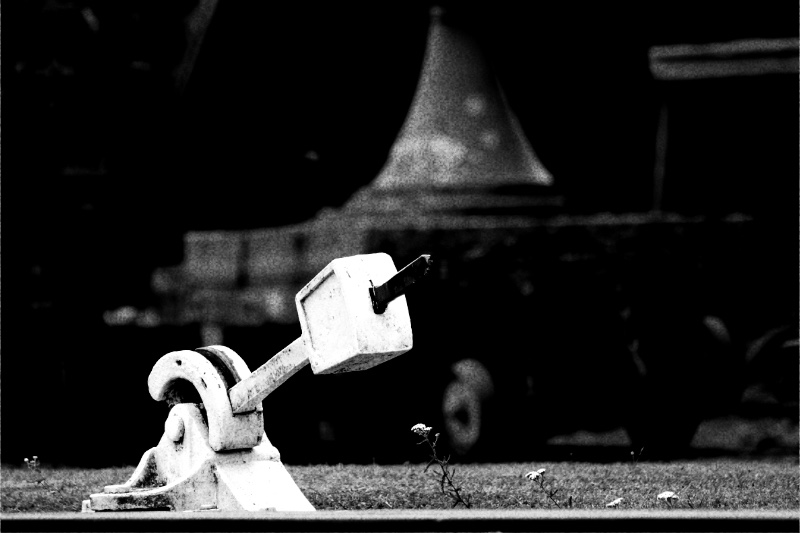 A railway points lever beside a locomotive, in high contrast black and white with coarse grain