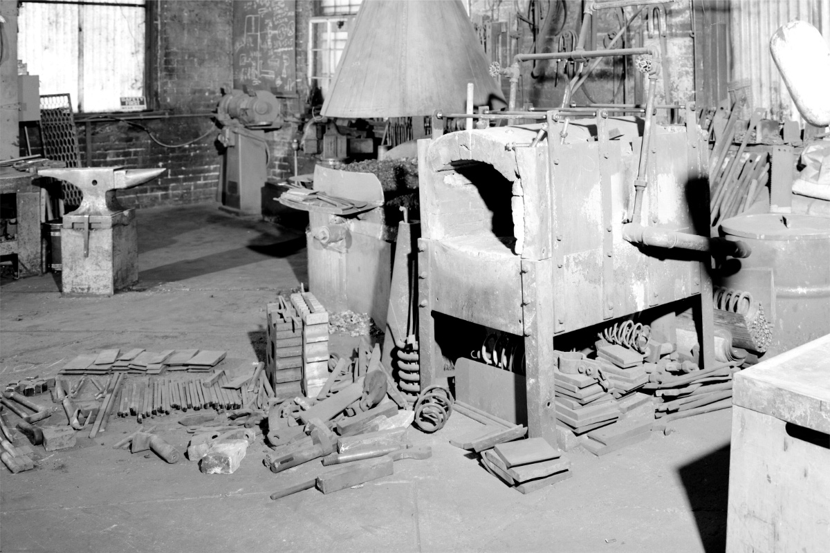 The interior of a blacksmith's shop with an anvil, forge and tools laid out, in plain black and white