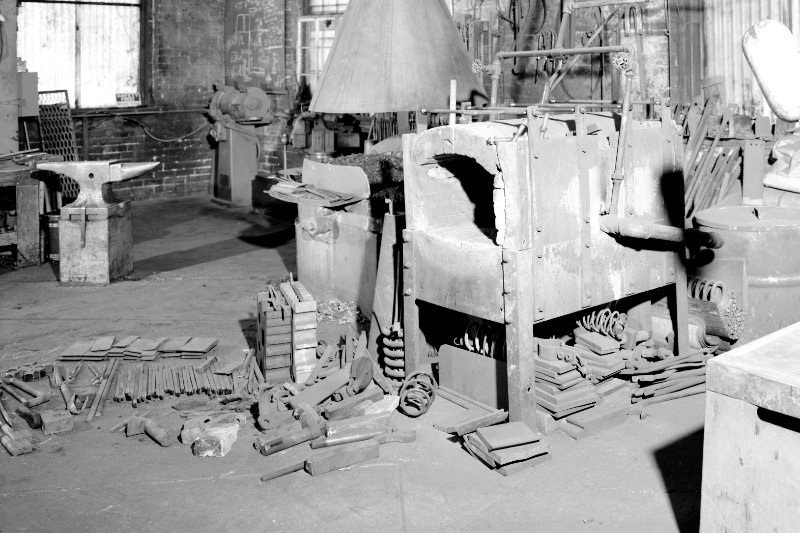 The interior of a blacksmith's shop with an anvil, forge and tools laid out, in plain black and white