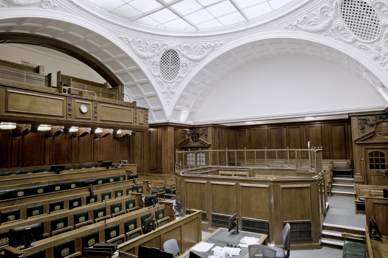 Empty ornate courtroom interior with wooden paneling and green seats