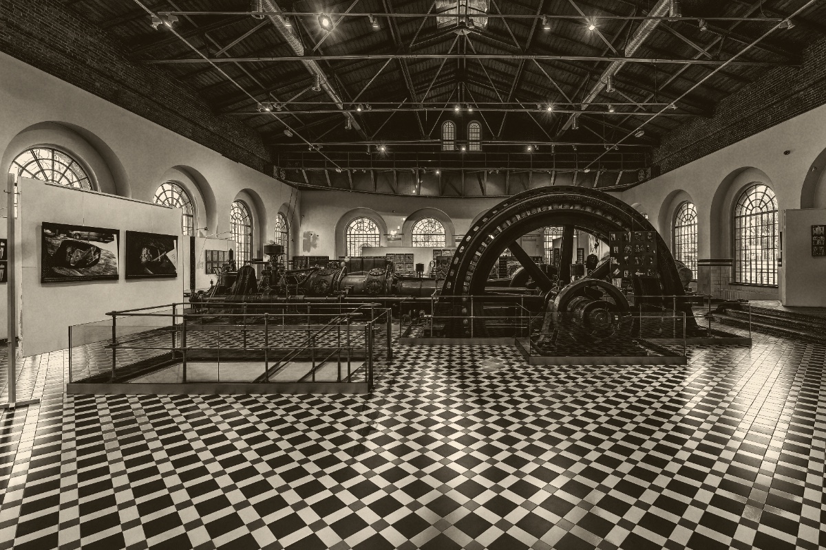 A machinery hall with a large flywheel and a checkerboard floor, in a warm duotone