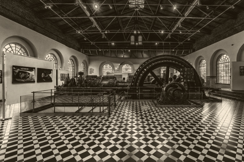 A machinery hall with a large flywheel and a checkerboard floor, in a warm duotone