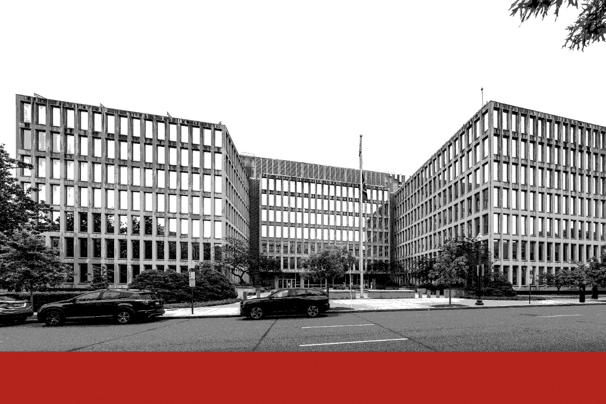 The rectilinear concrete and glass facade of the Theodore Roosevelt Building in Washington with flags outside, a deep band running across the foot of the frame