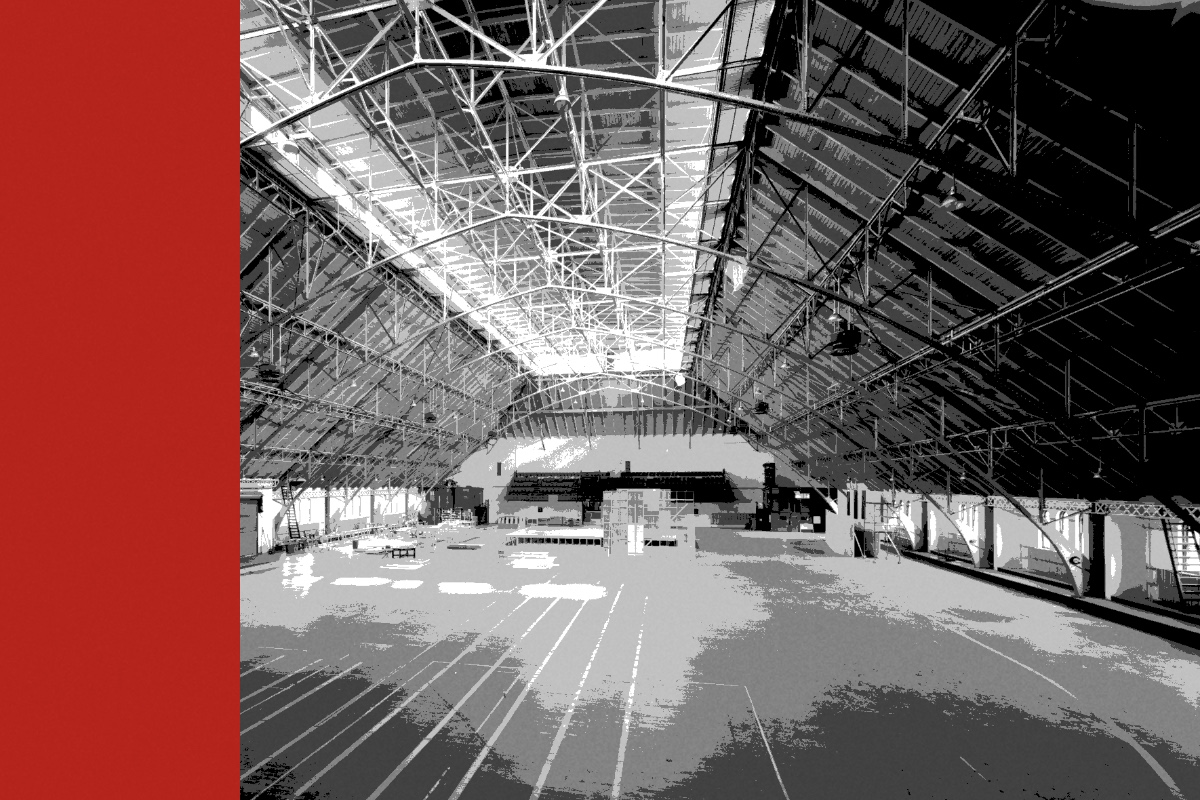 The interior of an empty armory drill hall with a steel truss roof, banded in the house treatment