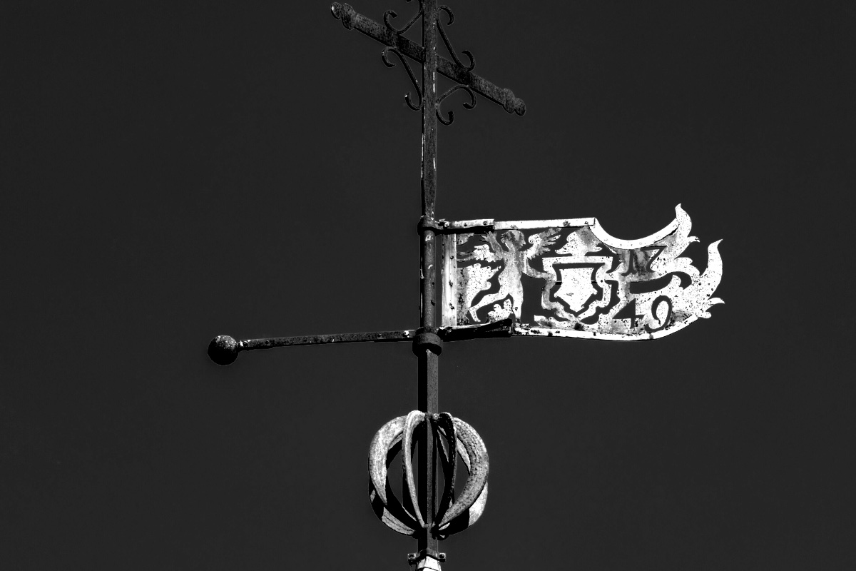 A wrought iron weather vane against a clear sky, in plain black and white