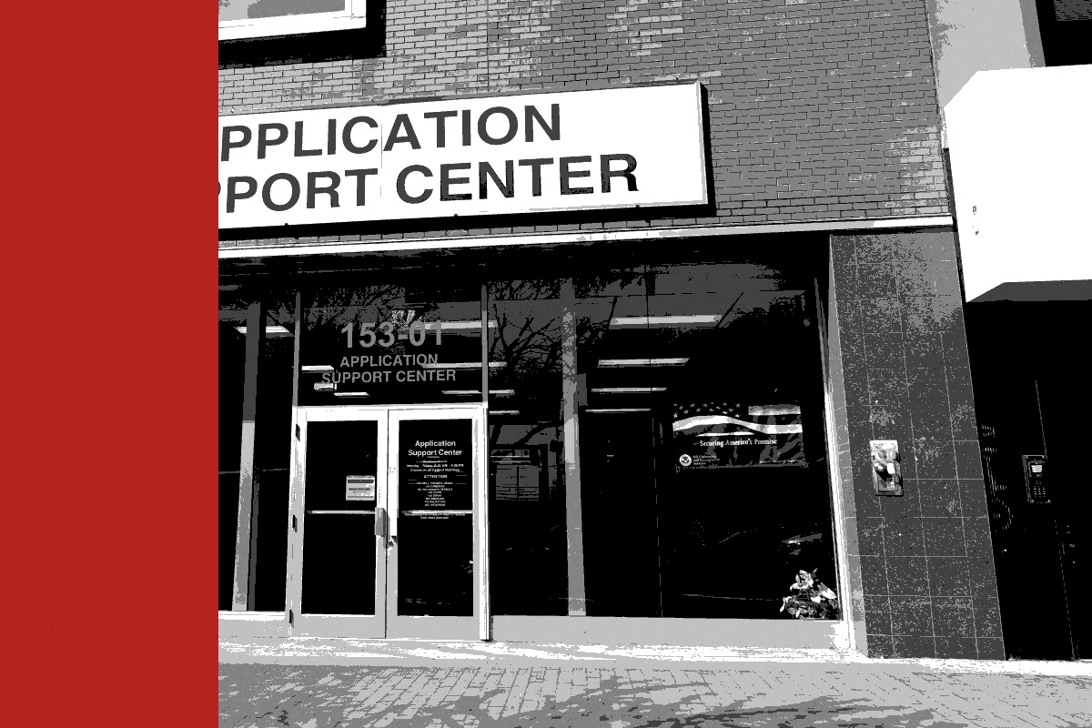 The storefront of a USCIS Application Support Center on Jamaica Avenue in Queens, a large sign above glass doors and windows, in near black and white with a flat red band down the left edge