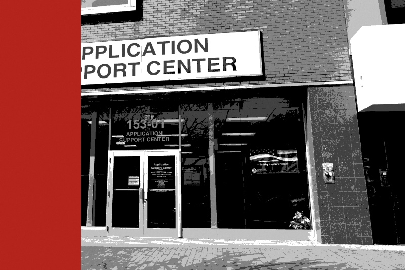 The storefront of a USCIS Application Support Center on Jamaica Avenue in Queens, a large sign above glass doors and windows, in near black and white with a flat red band down the left edge