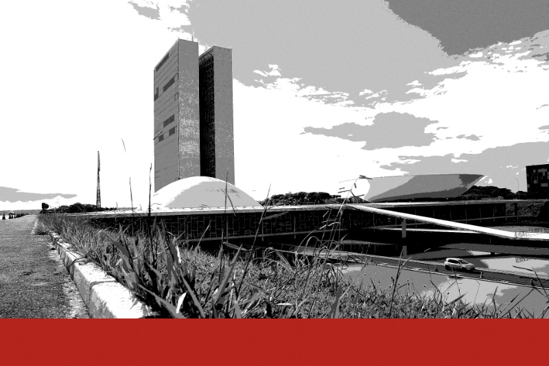 The National Congress in Brasilia seen from a grass verge beside a road, two tall office towers above a low white dome and an upturned bowl, with a reflecting pool to the right, in near black and white with a flat red band along the foot of the frame