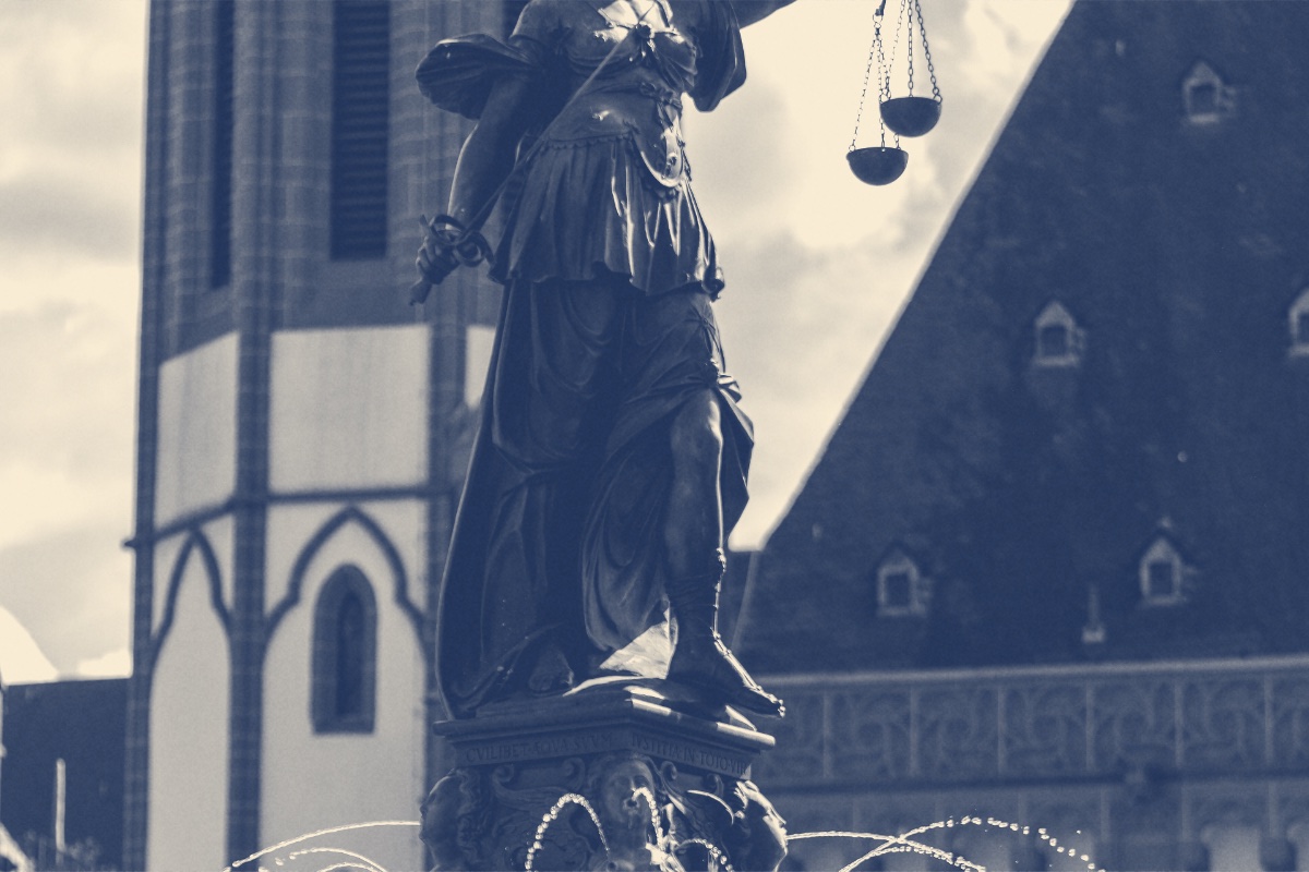 A bronze figure of Justice holding scales above a fountain, in a blue duotone