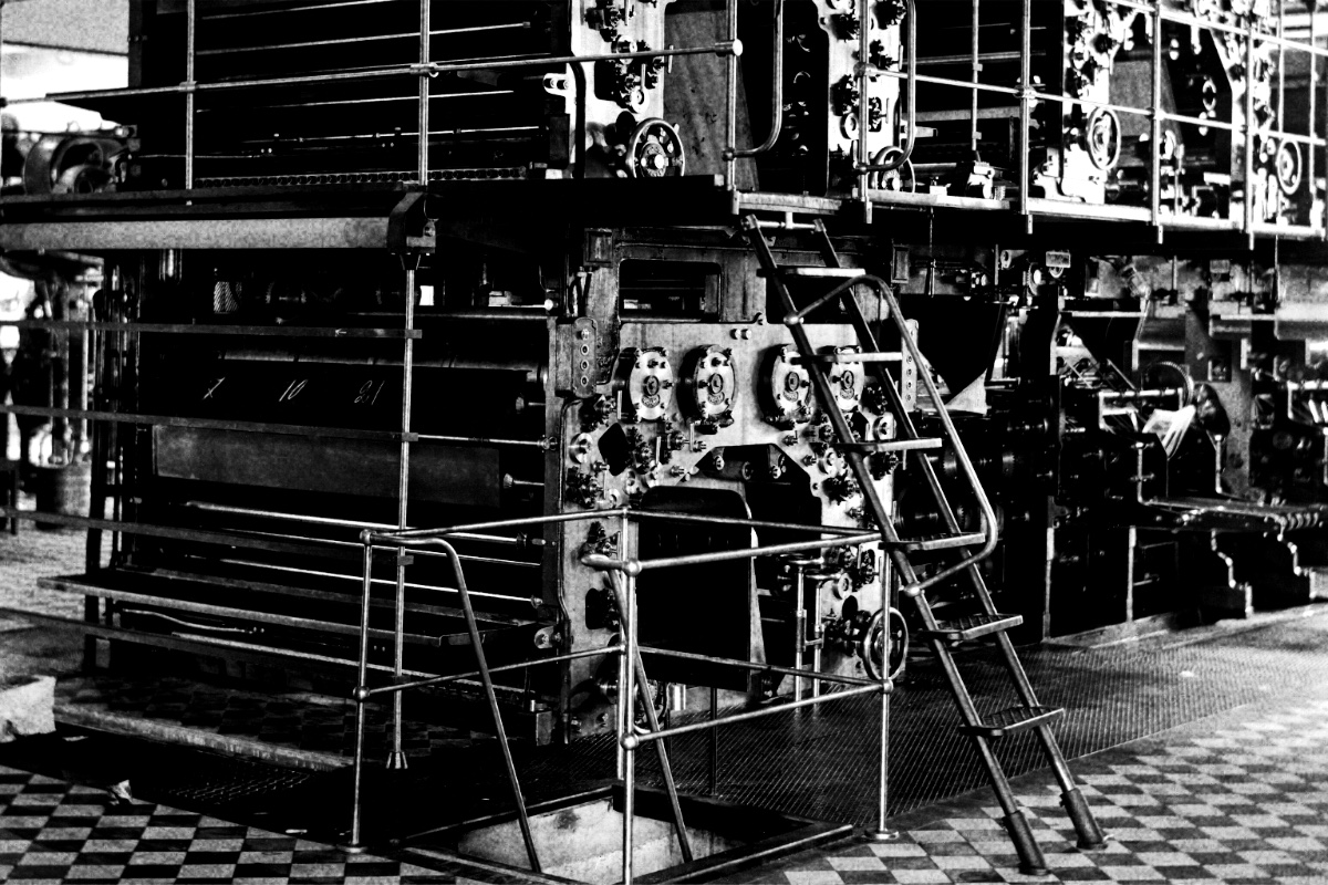 A large rotary printing press in a press hall, in high contrast black and white with coarse grain